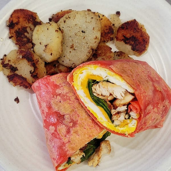 A red tortilla wrap filled with chicken, egg, and spinach, served with roasted potatoes.