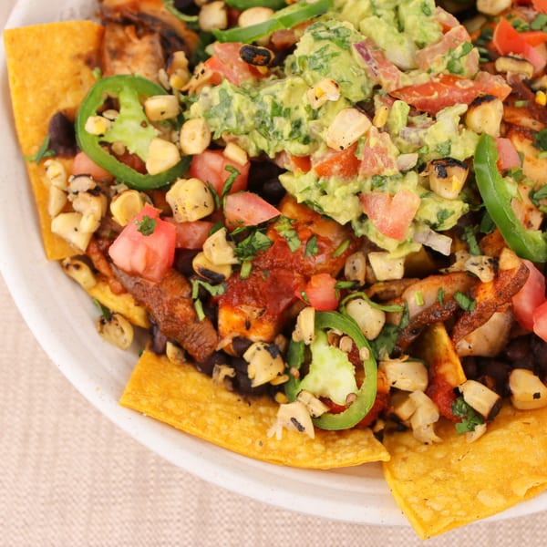 Close-up of loaded nachos with guacamole, tomatoes, corn, black beans, and jalapeños.