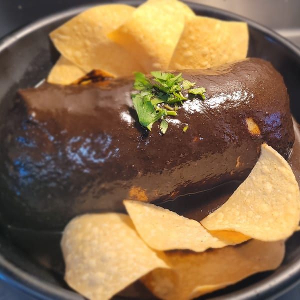 A dark brown mole burrito topped with cilantro and surrounded by tortilla chips in a black bowl.