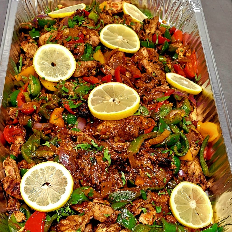 A large foil tray filled with seasoned chicken, colorful bell peppers, onions, and lemon slices.